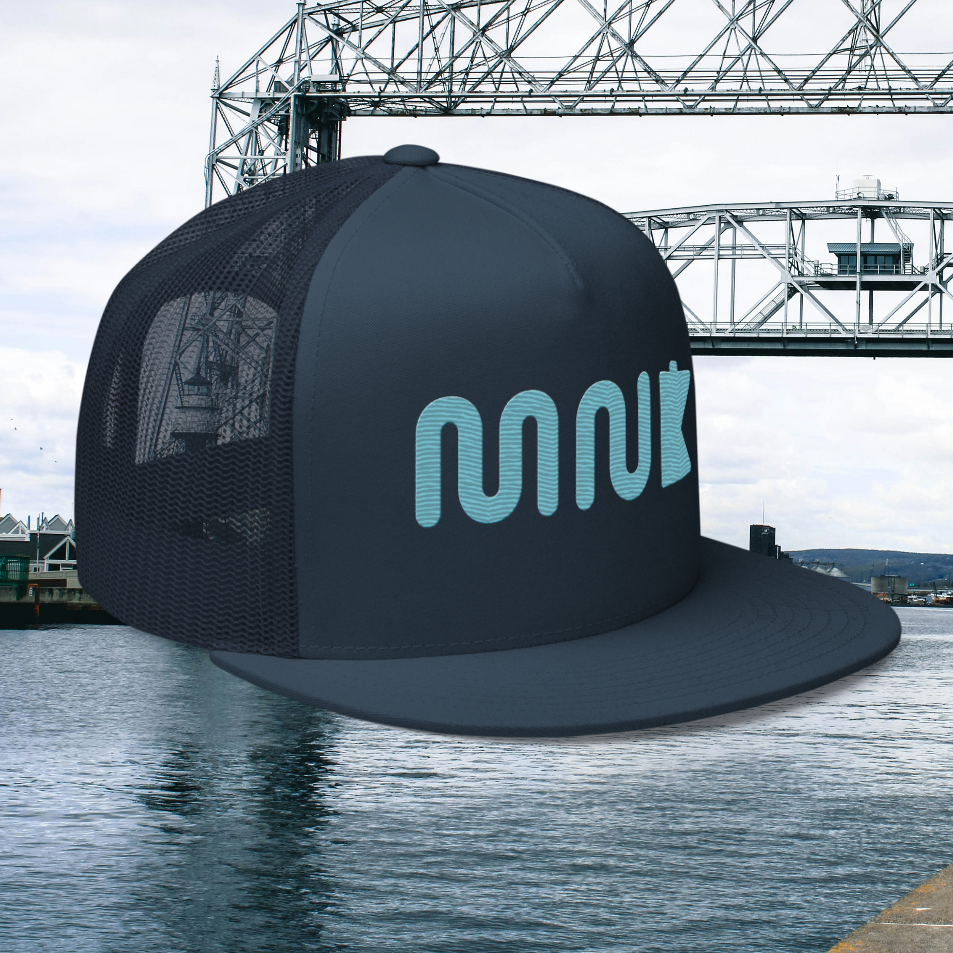 Minnesota hat with a blue "MN" using a wavy, river like font. There is a simplified blue outline of the state of Minnesota next to it. The midnight navy hat appears to be hovering over a photo of the aerial lift bridge in Duluth Minnesota.