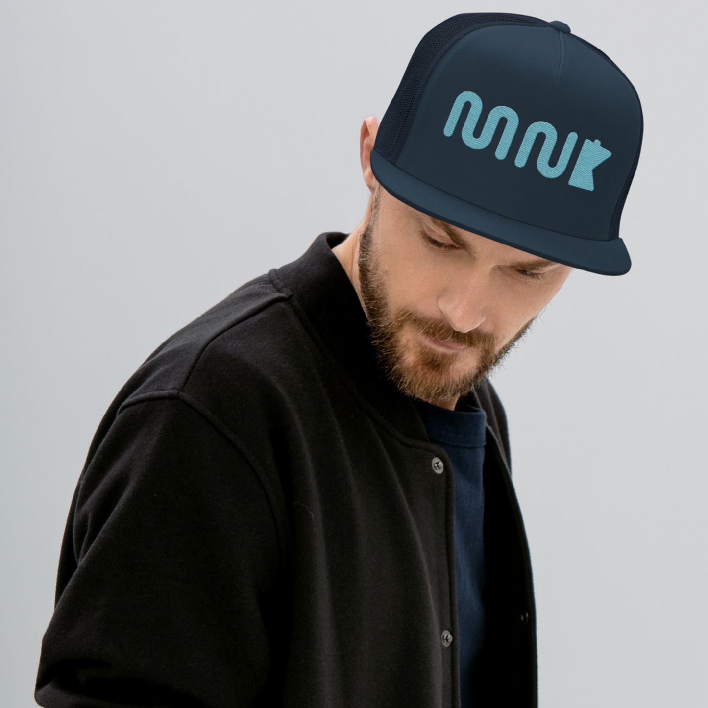 Man wearing a snapback hat. Minnesota hat with a blue "MN" using a wavy, river like font. There is a simplified blue outline of the state of Minnesota next to it. The midnight navy hat appears to be hovering over a photo of the aerial lift bridge in Duluth Minnesota.